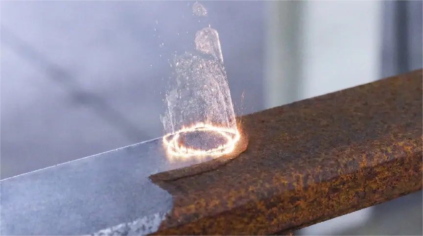 Close-up of laser rust removal in progress on a round steel bar